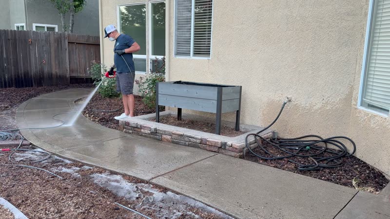Pressure washing a backyard concrete walkway beside a house