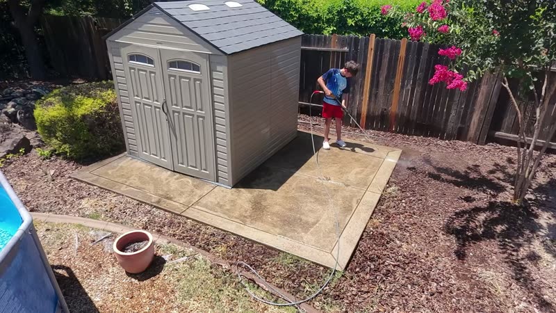 Harrison Cable pressure washing a backyard shed pad