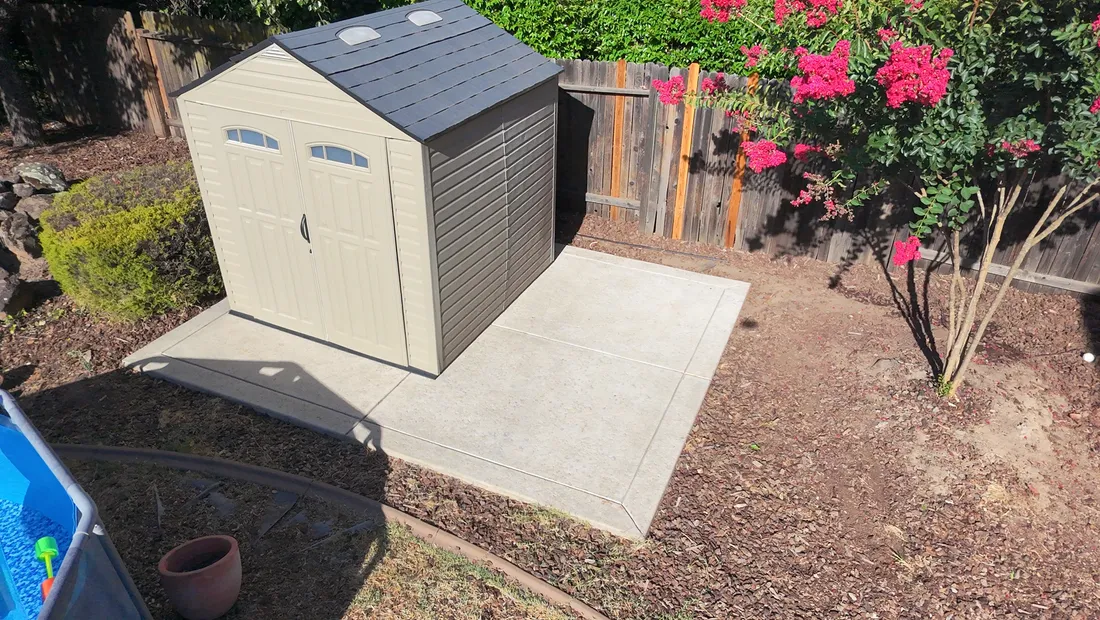 Clean concrete pad around a backyard shed after pressure washing