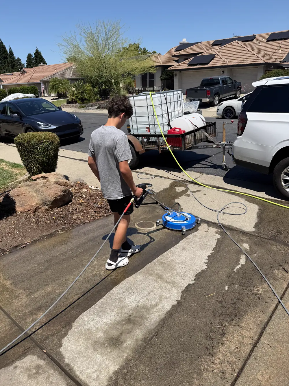 Crew member running a round surface cleaner across a dirty driveway, leaving a visibly clean band behind it