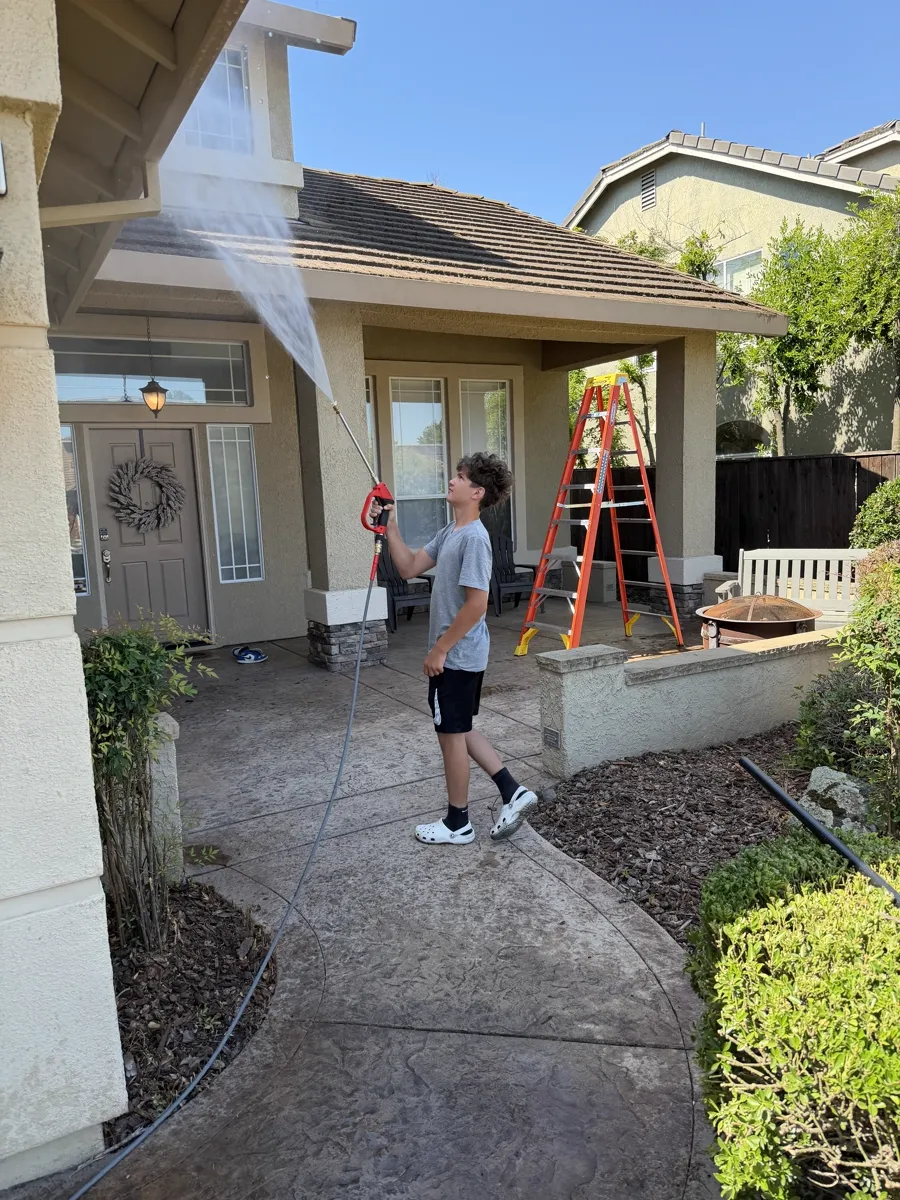 Cable crew member rinsing at the roofline with a ladder staged during a gutter cleaning visit