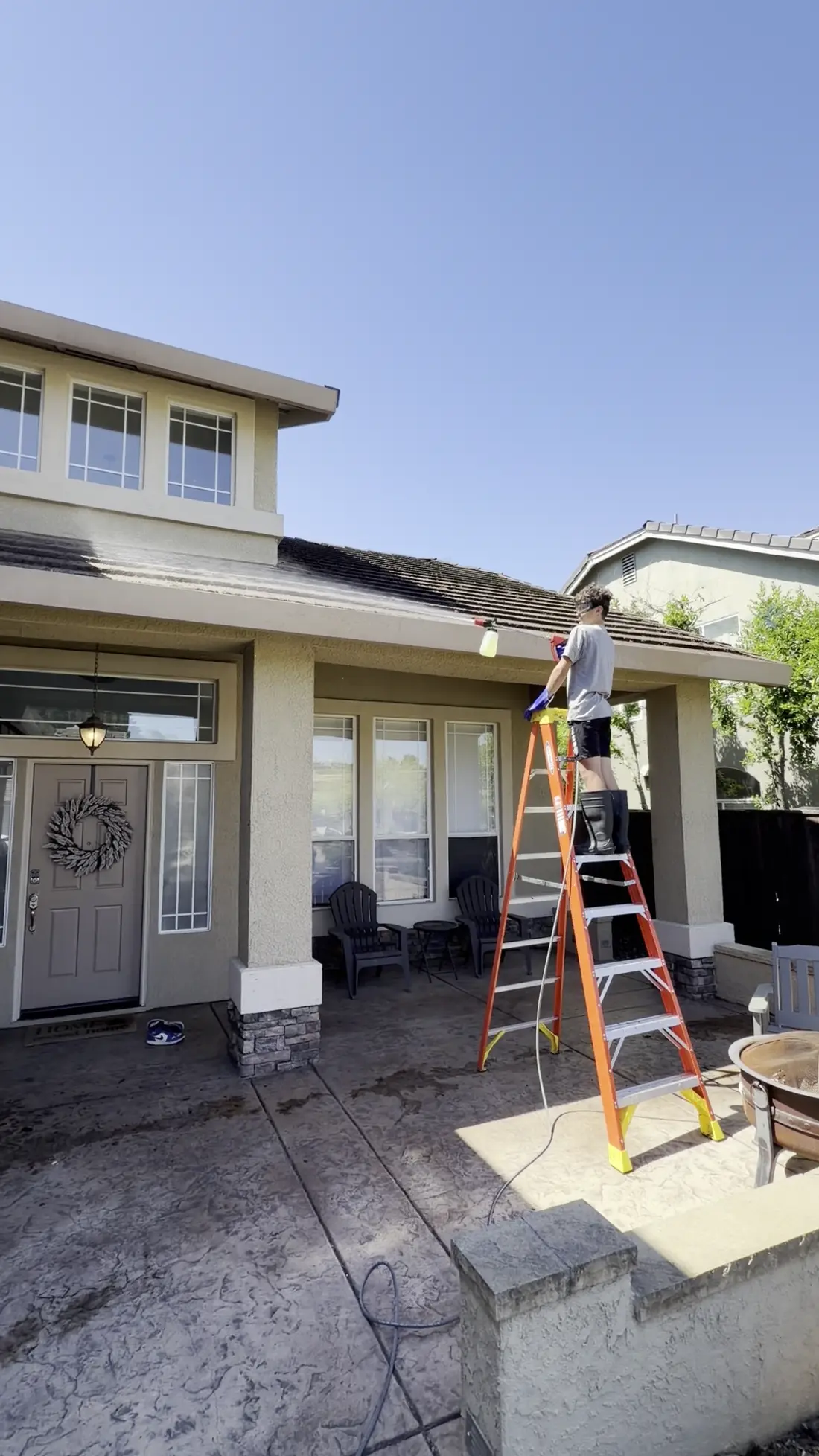 Crew member on a ladder applying cleaning solution to the low tile roof over a front porch