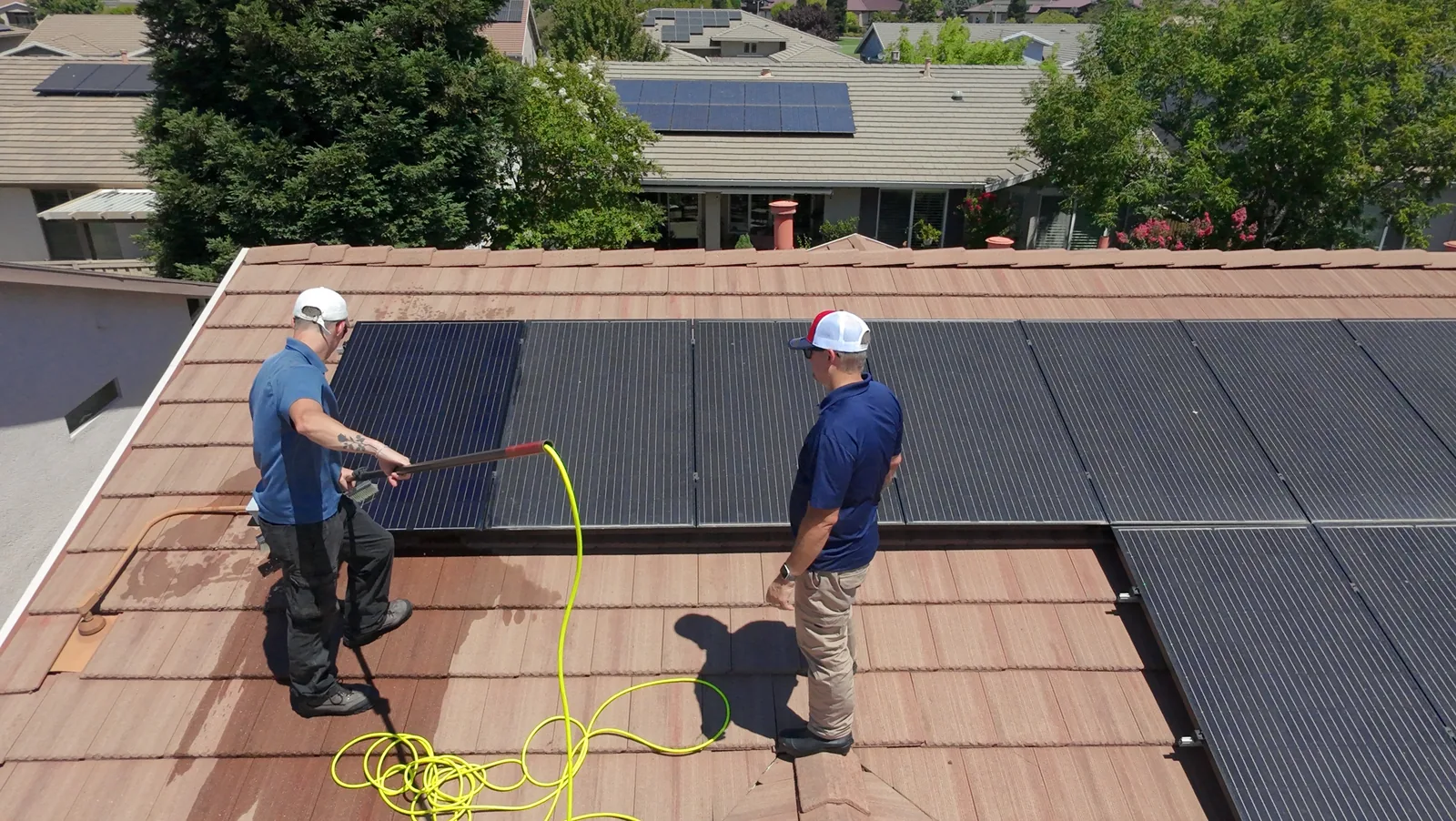 Two Cable Pressure Washing crew members on a tile roof washing a solar array with a water-fed pole brush