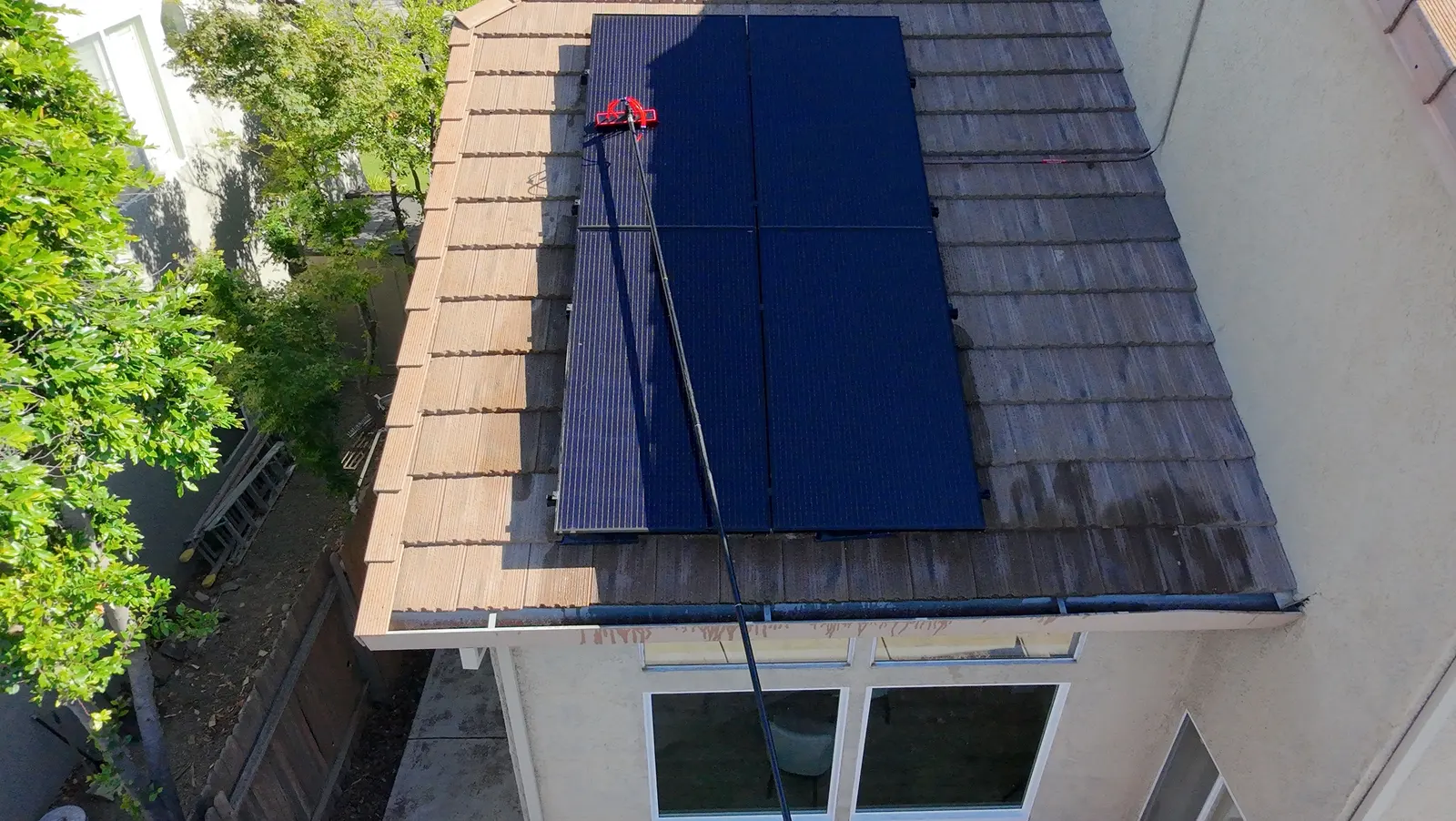 Solar panel cleaning on a two-story home, water-fed pole reaching a roof-mounted array from below